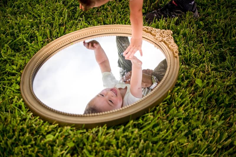 Child reaching for their reflection in a mirror